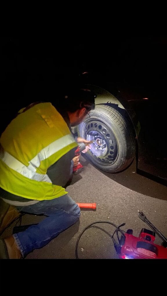“Technician providing emergency mobile tyre fitting service at night for a stranded car”